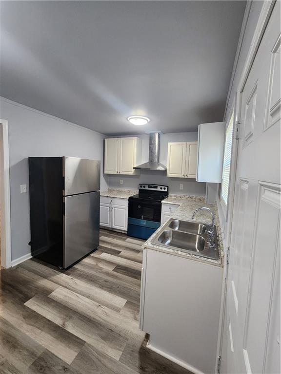 kitchen featuring white cabinetry, wall chimney range hood, stainless steel appliances, light hardwood / wood-style floors, and sink