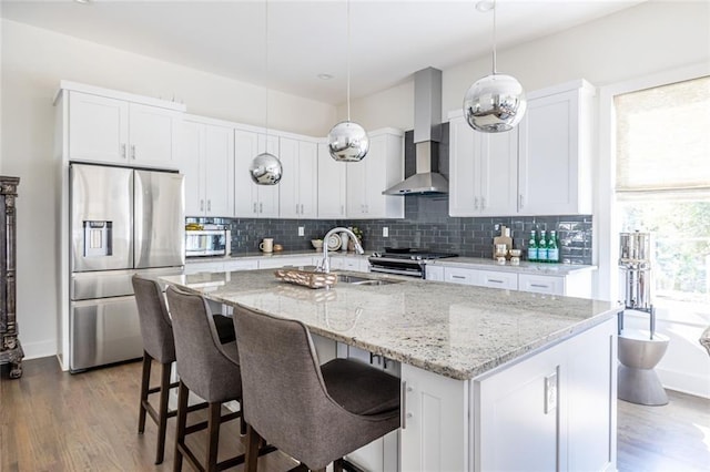 kitchen with stainless steel appliances, an island with sink, white cabinets, and wall chimney exhaust hood