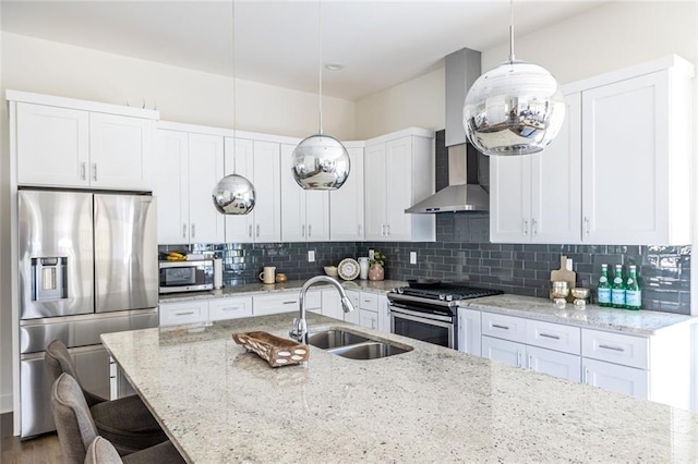 kitchen with pendant lighting, wall chimney range hood, sink, appliances with stainless steel finishes, and white cabinetry