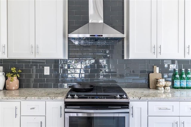 kitchen featuring white cabinets, light stone countertops, stainless steel gas range oven, and wall chimney range hood