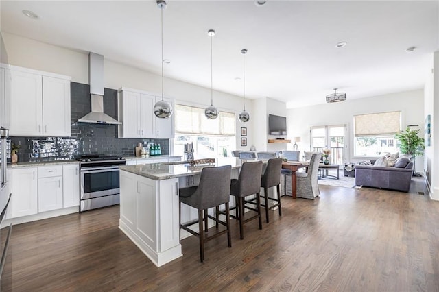 kitchen featuring stainless steel range oven, a center island, dark stone countertops, wall chimney range hood, and white cabinets