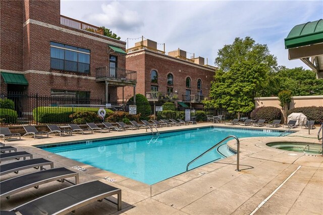 community pool with fence, a hot tub, and a patio area