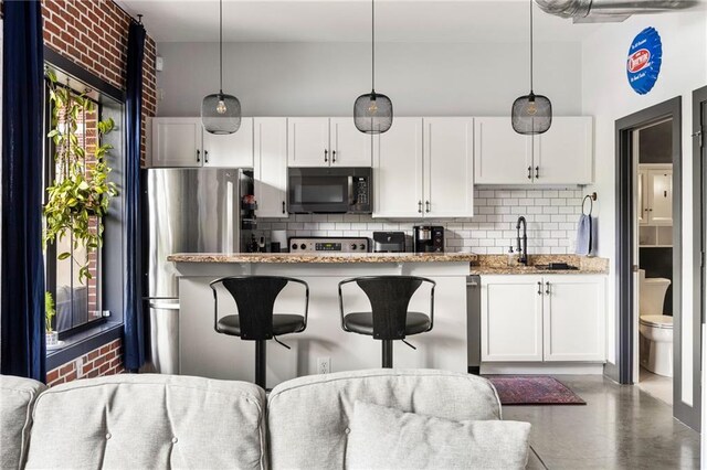kitchen featuring white cabinets, a sink, stainless steel appliances, decorative backsplash, and a kitchen bar