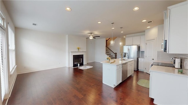 kitchen featuring white cabinetry, stainless steel appliances, an island with sink, ceiling fan, and dark wood-type flooring