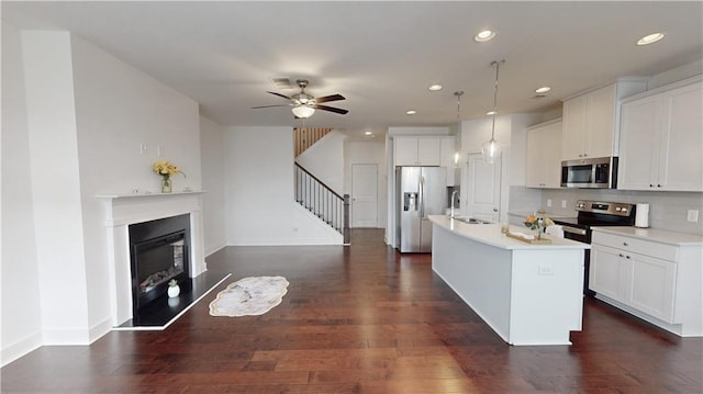 kitchen featuring decorative light fixtures, dark hardwood / wood-style flooring, ceiling fan, appliances with stainless steel finishes, and a center island with sink