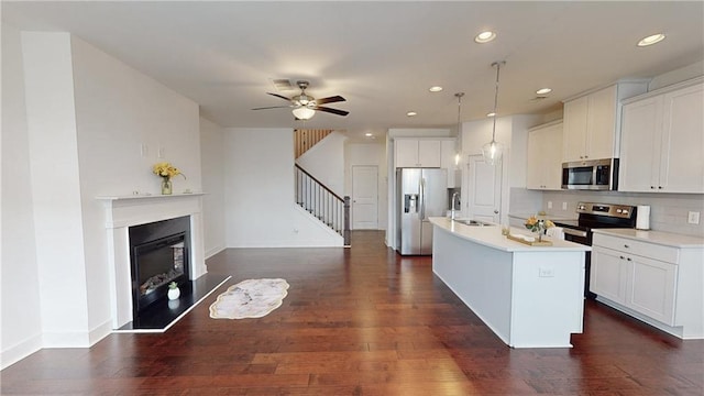 kitchen with a sink, light countertops, dark wood-style floors, stainless steel appliances, and an island with sink