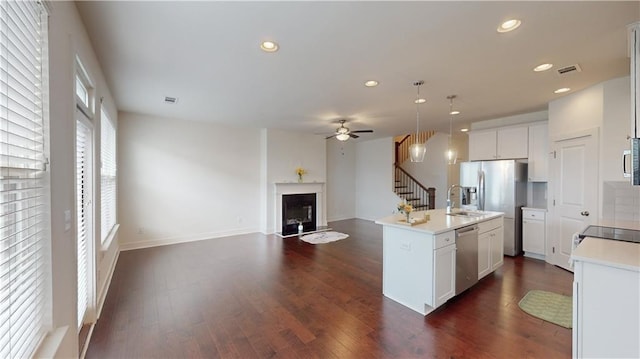 kitchen with dark hardwood / wood-style floors, decorative light fixtures, a center island with sink, stainless steel appliances, and ceiling fan