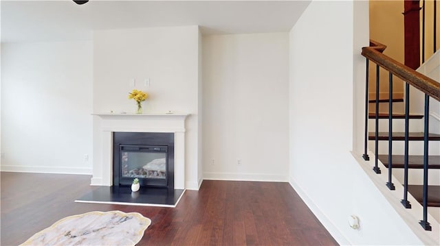 living area featuring baseboards, a glass covered fireplace, wood finished floors, and stairway