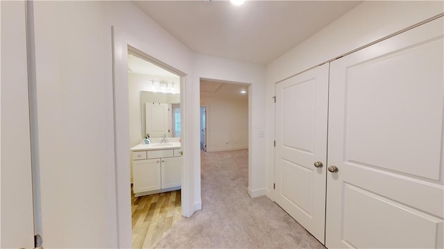 hall with light wood-style floors, a sink, and baseboards