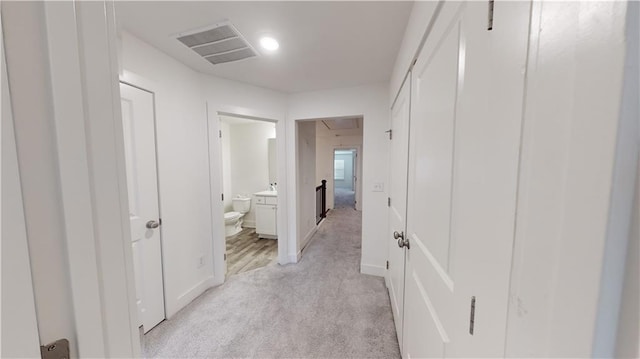 hallway featuring light colored carpet, baseboards, visible vents, and attic access