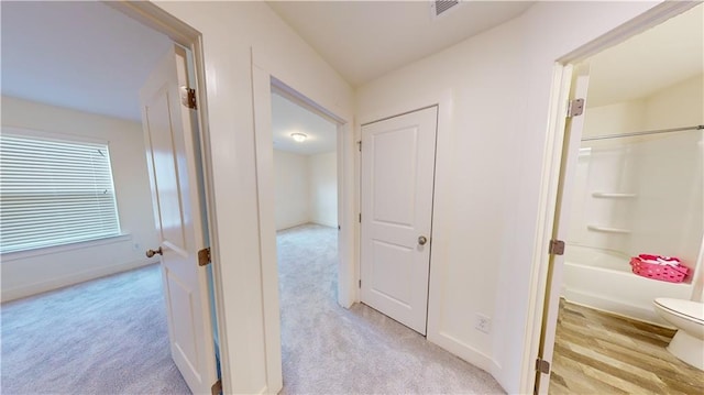 hall with baseboards, light colored carpet, and visible vents