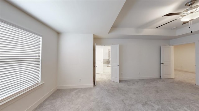 unfurnished bedroom featuring ceiling fan, light colored carpet, baseboards, ensuite bathroom, and a tray ceiling