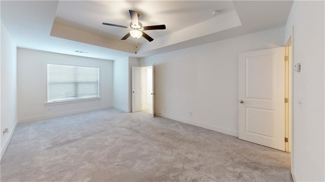 unfurnished bedroom with ceiling fan, carpet floors, baseboards, a tray ceiling, and visible vents