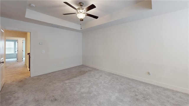 carpeted empty room featuring baseboards, a ceiling fan, a tray ceiling, and visible vents