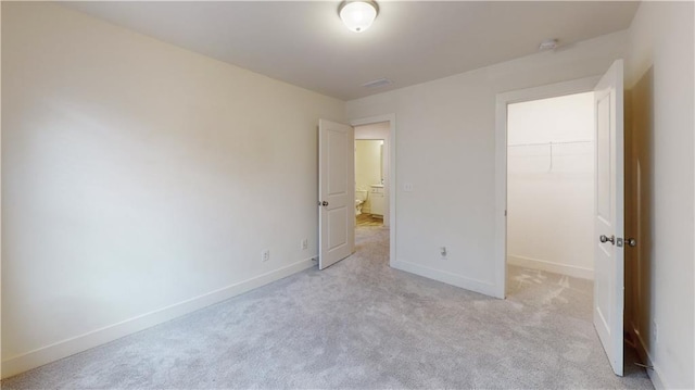 unfurnished bedroom with visible vents, a closet, baseboards, a walk in closet, and light colored carpet