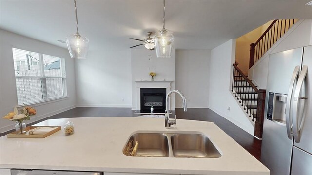 kitchen with ceiling fan, stainless steel refrigerator with ice dispenser, a fireplace with flush hearth, a sink, and light countertops