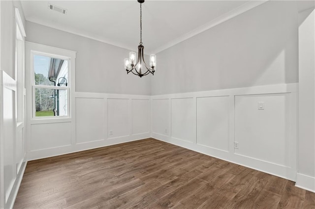 unfurnished dining area with wood-type flooring, an inviting chandelier, and crown molding