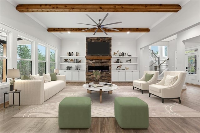 living room featuring built in shelves, light hardwood / wood-style floors, a stone fireplace, and beam ceiling