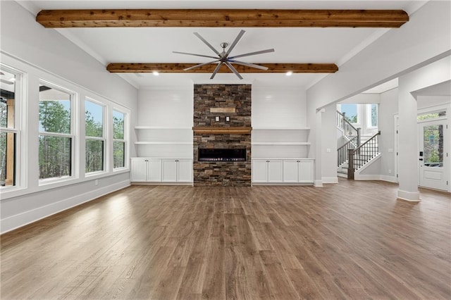 unfurnished living room featuring a stone fireplace, ceiling fan, beamed ceiling, and hardwood / wood-style flooring