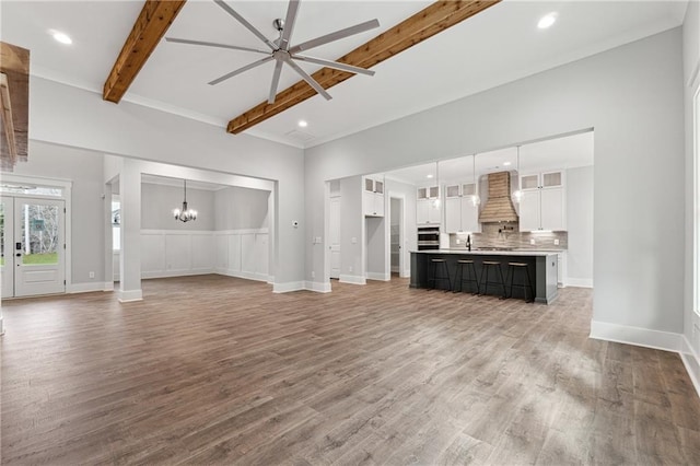 unfurnished living room with beamed ceiling, ceiling fan with notable chandelier, and hardwood / wood-style floors