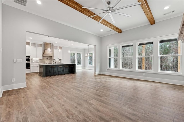 unfurnished living room with beamed ceiling, wood-type flooring, and ceiling fan with notable chandelier