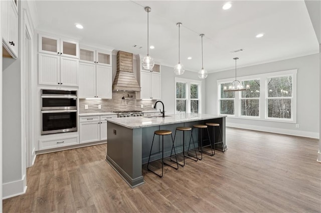 kitchen with white cabinetry, sink, an island with sink, and custom exhaust hood