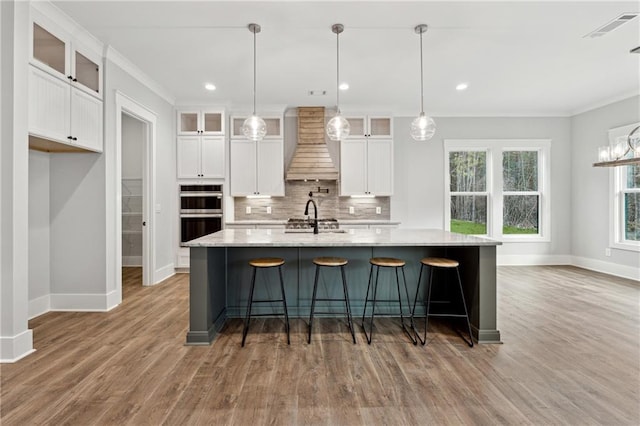 kitchen featuring decorative light fixtures, white cabinetry, custom range hood, and a kitchen island with sink