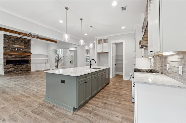 kitchen featuring sink, hanging light fixtures, high end stove, a kitchen island with sink, and white cabinets