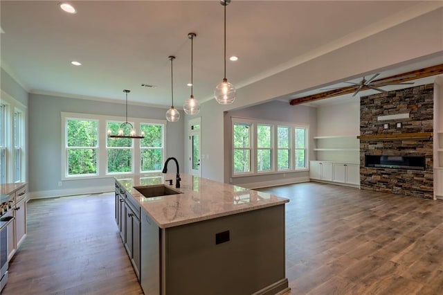6449 Snelling Mill Rd, Flowery Branch, GA 30542 - kitchen featuring a sink, a stone fireplace, light stone counters, wood finished floors, and a center island with sink