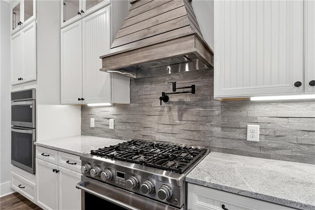 kitchen featuring premium range hood, white cabinets, light stone countertops, appliances with stainless steel finishes, and tasteful backsplash