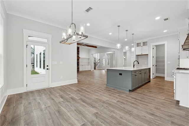 kitchen with crown molding, sink, white cabinets, hanging light fixtures, and an island with sink