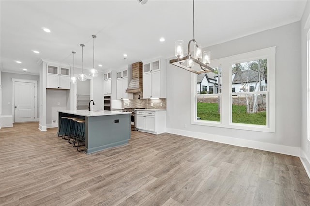 kitchen featuring pendant lighting, sink, custom range hood, stainless steel range oven, and white cabinetry