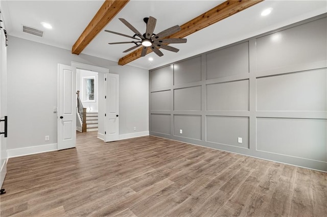 unfurnished bedroom featuring beam ceiling, a barn door, light hardwood / wood-style floors, and ceiling fan