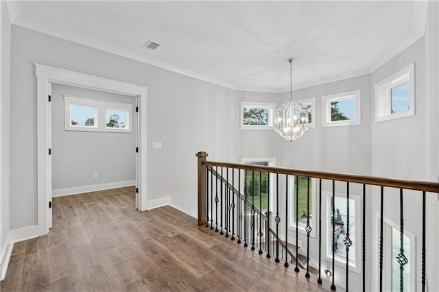 hallway featuring hardwood / wood-style flooring, crown molding, and an inviting chandelier