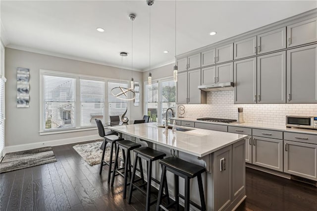 kitchen with sink, gray cabinetry, crown molding, hanging light fixtures, and an island with sink