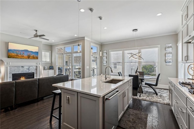 kitchen featuring sink, appliances with stainless steel finishes, hanging light fixtures, a high end fireplace, and a center island with sink