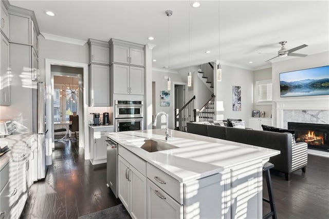 kitchen with sink, hanging light fixtures, gray cabinets, a fireplace, and a kitchen island with sink