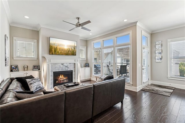 living room with ornamental molding, dark wood-type flooring, ceiling fan, and a high end fireplace