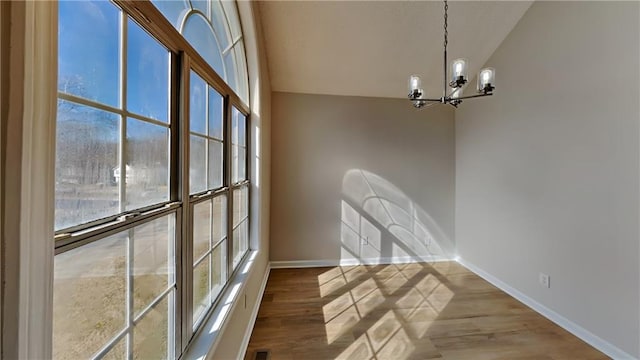 unfurnished dining area with an inviting chandelier, lofted ceiling, and hardwood / wood-style floors