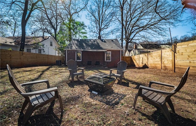 back of house featuring a fenced backyard, a fire pit, an outbuilding, and brick siding