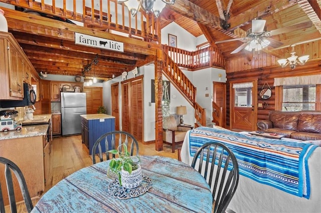 dining space with beam ceiling, rustic walls, wooden ceiling, ceiling fan with notable chandelier, and light wood-type flooring