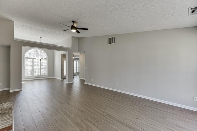 unfurnished living room featuring visible vents, baseboards, vaulted ceiling, ceiling fan with notable chandelier, and dark wood-style flooring