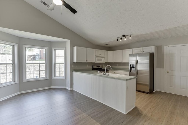 kitchen with a sink, stainless steel appliances, a peninsula, light wood finished floors, and lofted ceiling