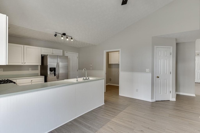 kitchen with light wood finished floors, lofted ceiling, a sink, a textured ceiling, and stainless steel fridge