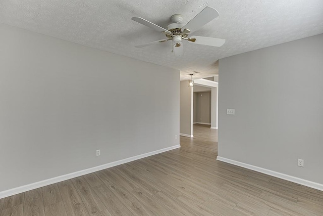 spare room featuring light wood finished floors, a textured ceiling, baseboards, and a ceiling fan