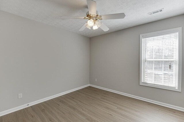 spare room featuring visible vents, a textured ceiling, baseboards, and wood finished floors