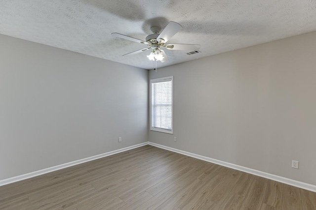 empty room featuring ceiling fan, visible vents, baseboards, and wood finished floors