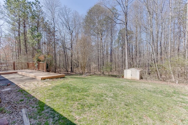 view of yard featuring a forest view, a wooden deck, an outbuilding, and a storage shed