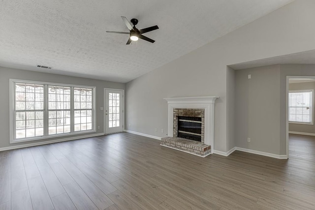 unfurnished living room featuring visible vents, ceiling fan, a fireplace, wood finished floors, and a textured ceiling