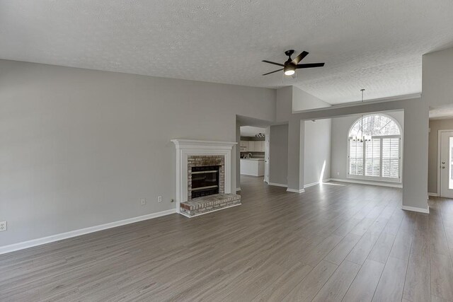 unfurnished living room featuring lofted ceiling, ceiling fan with notable chandelier, wood finished floors, a fireplace, and baseboards